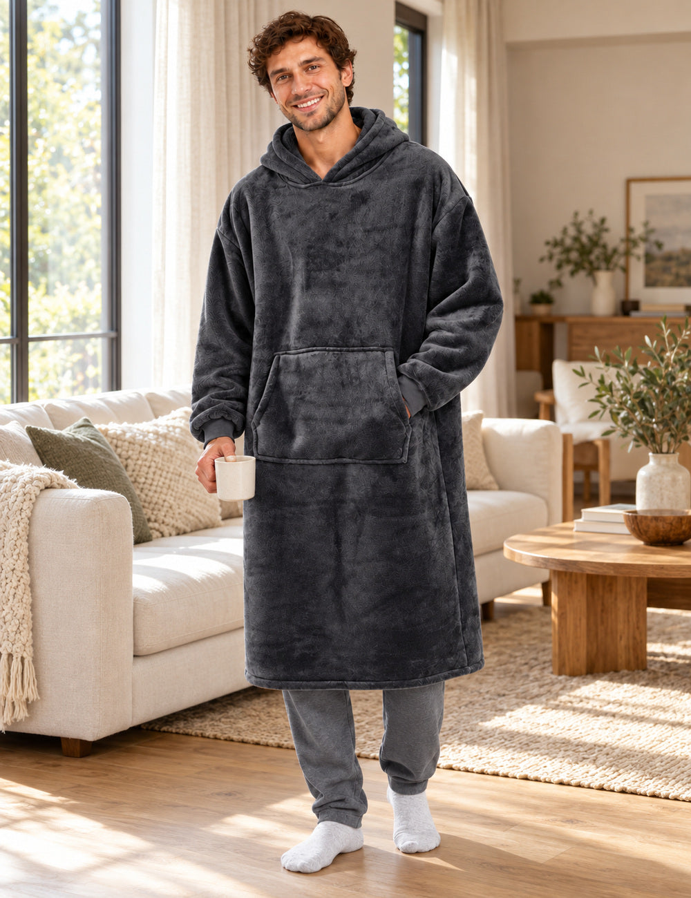 Sweat pull plaid homme gris foncé porté debout dans un salon lumineux, coupe longue et poche visibles