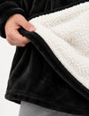 Main relevant le bas du Pull Plaid Polaire Homme noir pour montrer la doublure sherpa blanche et le tissu extérieur