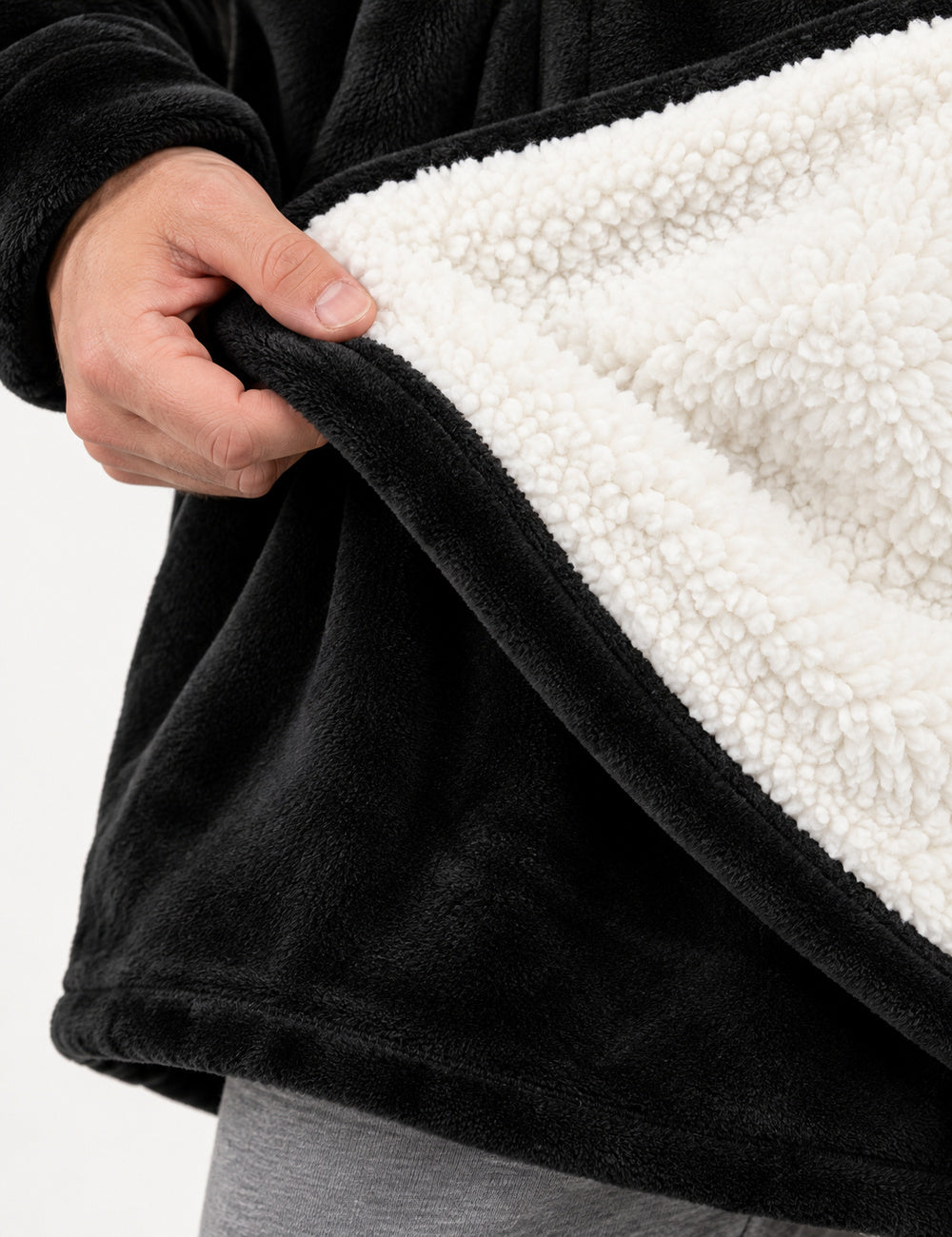 Main relevant le bas du Pull Plaid Polaire Homme noir pour montrer la doublure sherpa blanche et le tissu extérieur