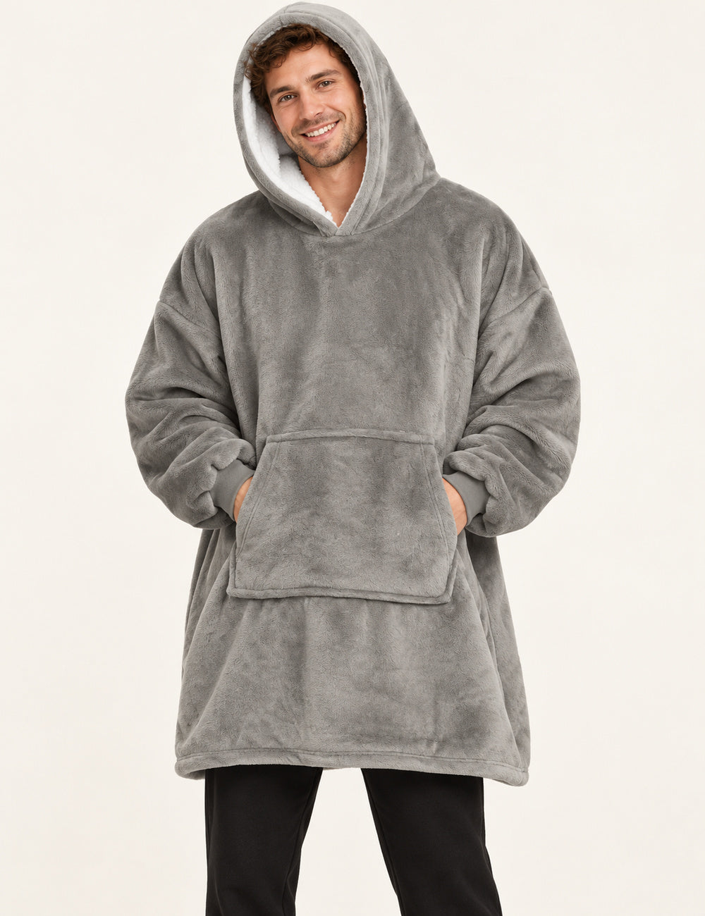 Pull Plaid Polaire Homme gris porté debout avec un pantalon noir, capuche doublée de sherpa blanche et mains dans la poche