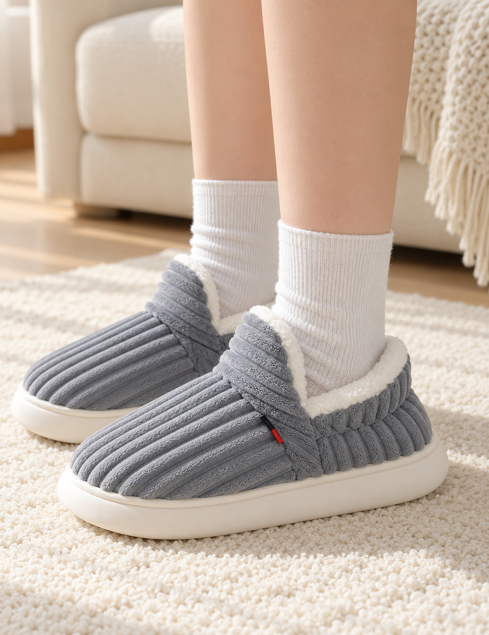Chaussons Alix gris portés avec des chaussettes blanches, les deux pieds posés sur un tapis