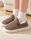 Chaussons Alix marron taupe portés avec des chaussettes blanches, pieds posés sur un tapis