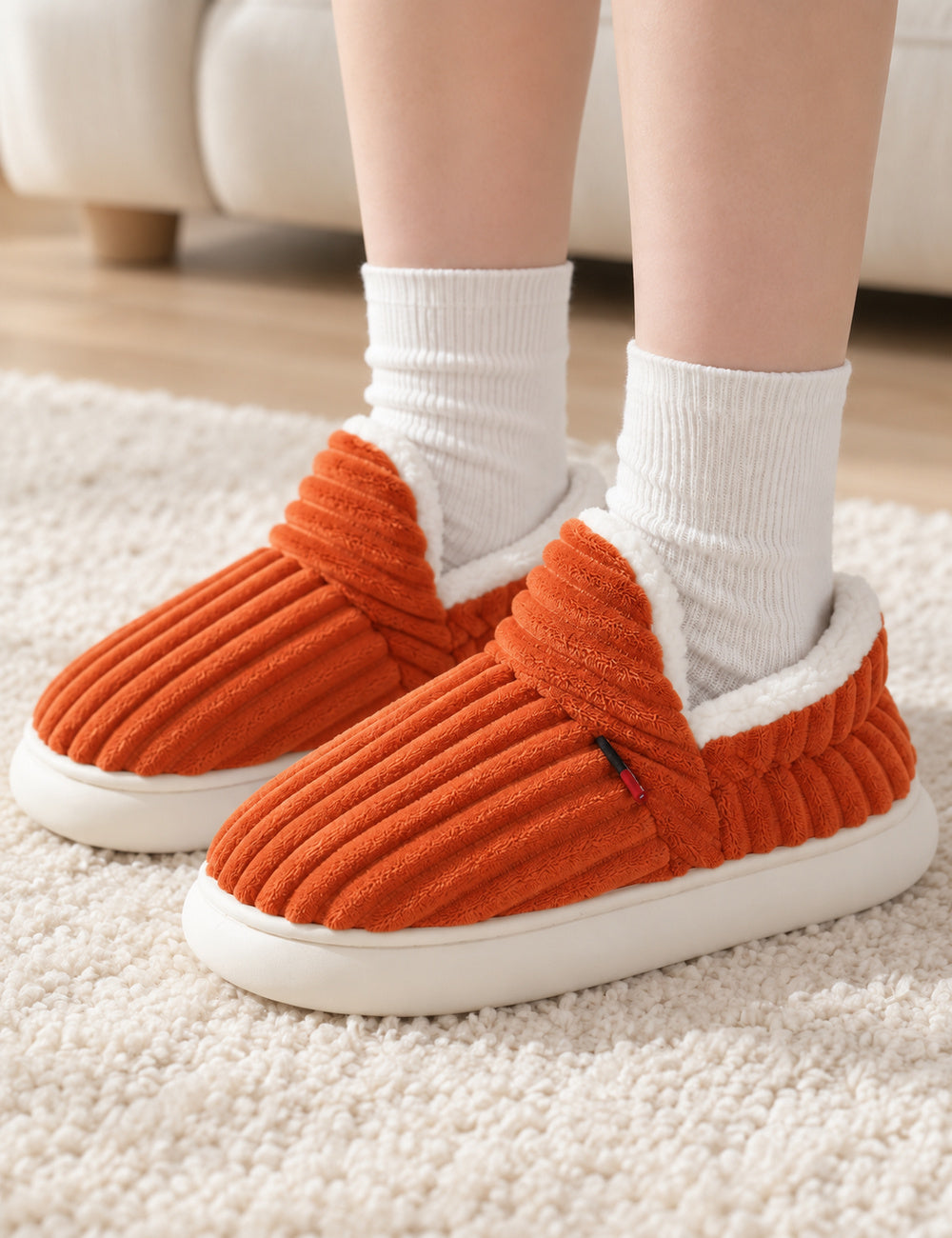 Chaussons Alix orange portés avec des chaussettes blanches, pieds posés sur un tapis