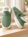 Chaussons Alix vert sauge vus de face et de côté sur un rebord en bois clair
